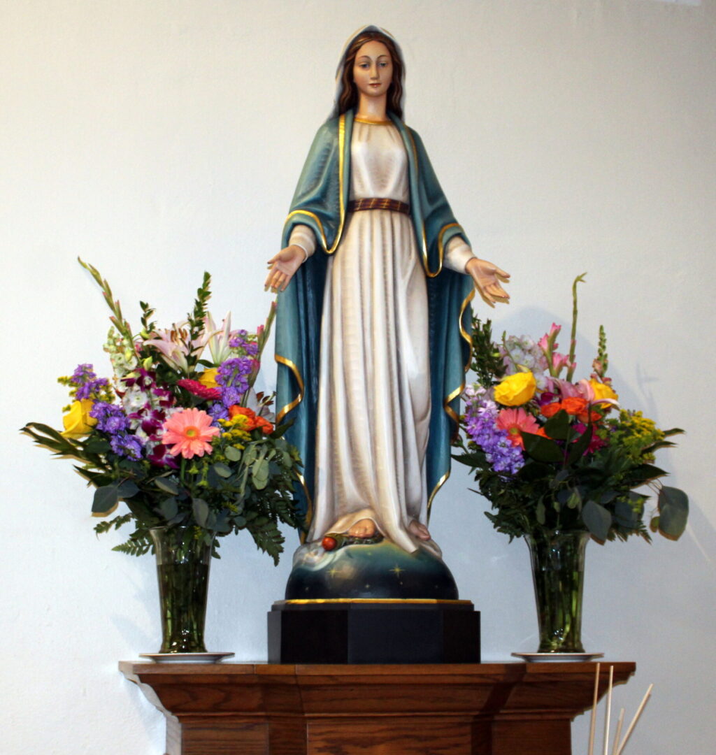 The statue of Mary with two vases of colorful flowers