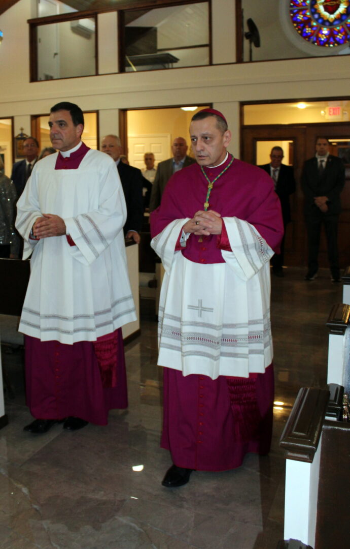 Two priests wearing a white and maroon uniform