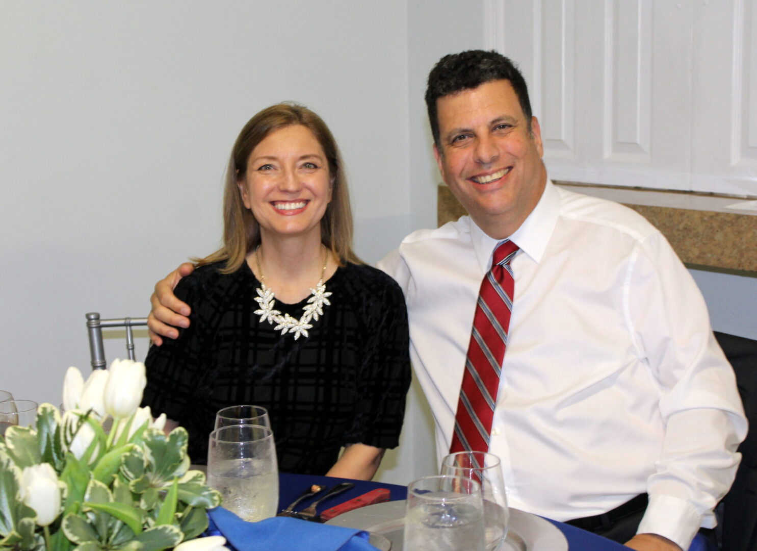 A man wearing a white polo and red tie and a woman wearing a black top with white necklace