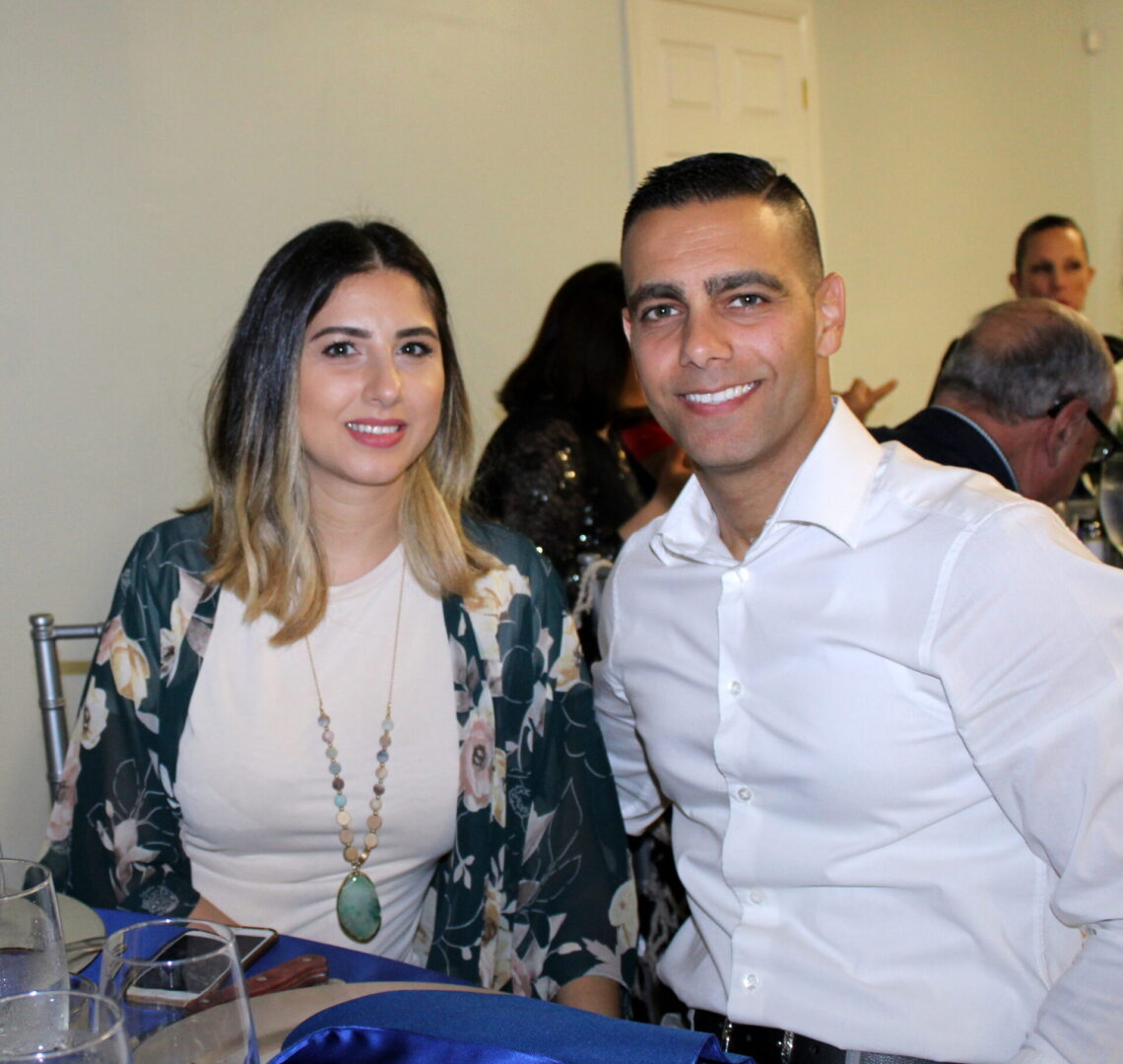 A man wearing a white polo with a clean-cut hair style and a woman wearing a white top with green floral cardigan