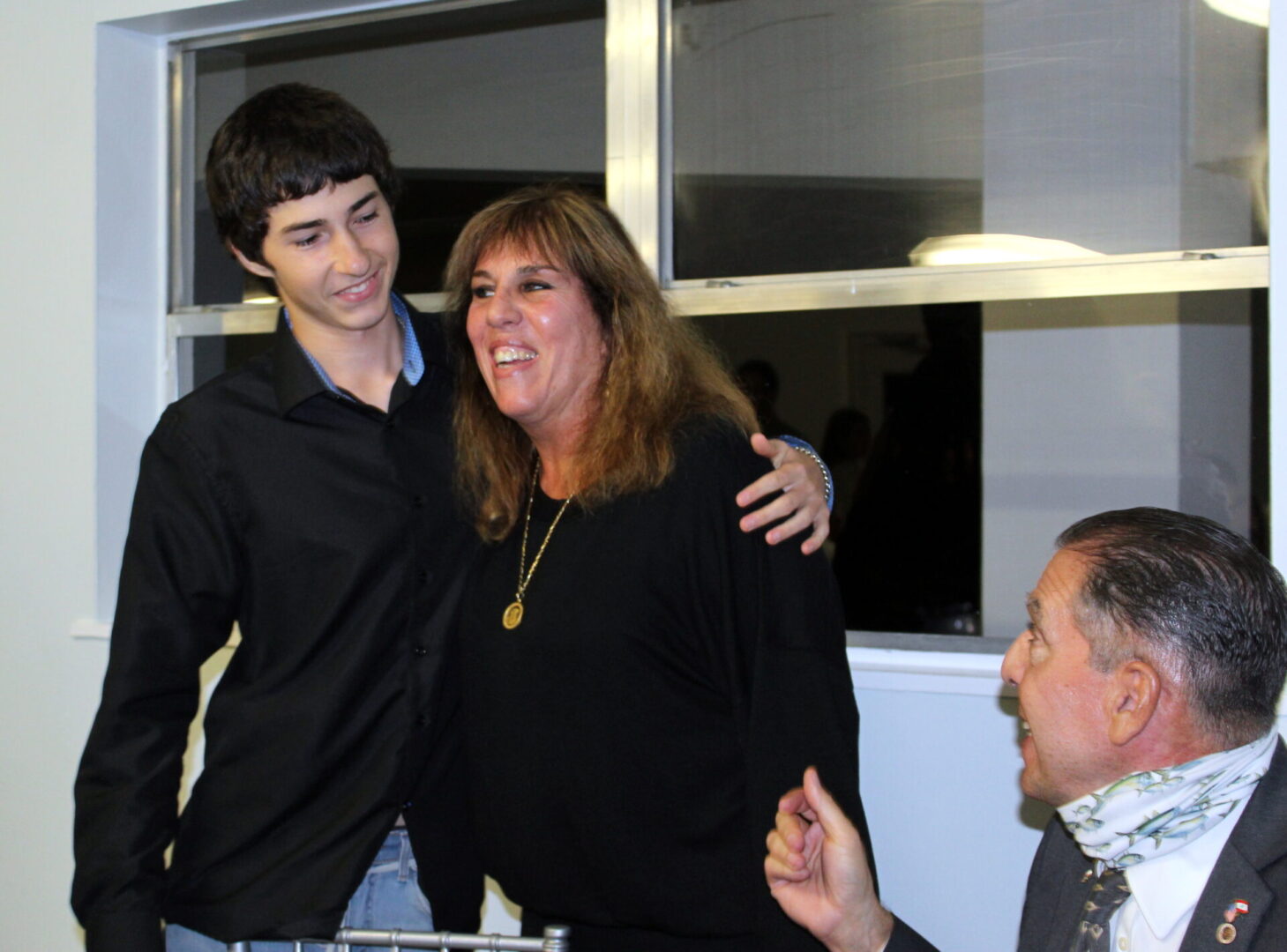 A woman wearing a plain black shirt with gold necklace and a man wearing a black polo