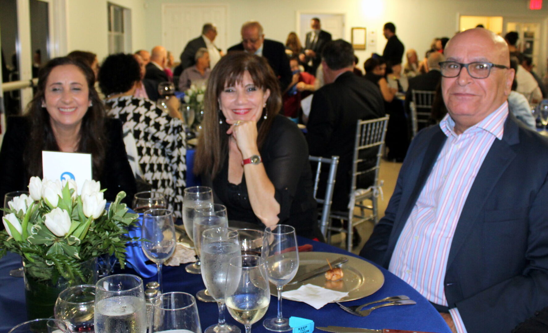 Two ladies wearing black top and a bald man wearing a blue suit