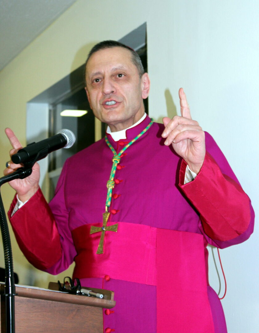 A church personnel wearing a purple attire with green cross on his neck