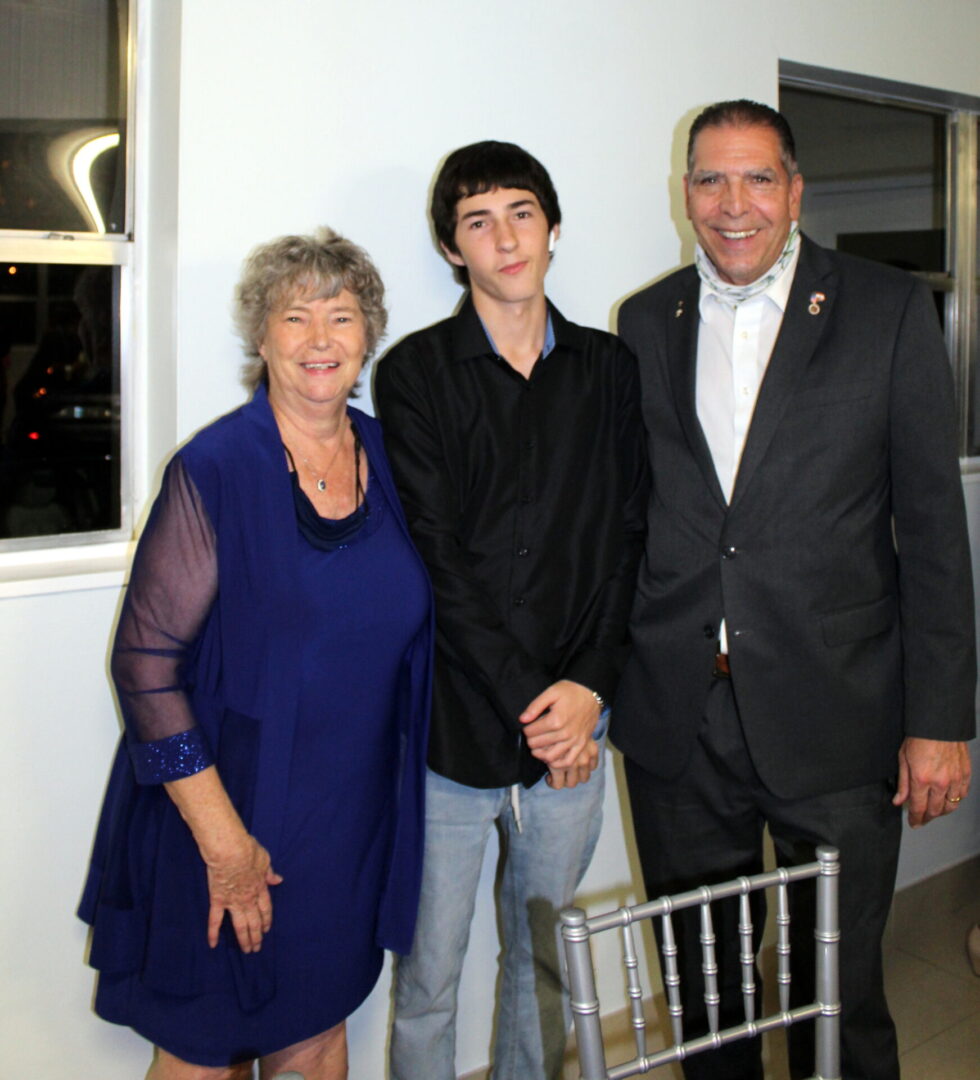 Two men wearing black suit and polo and a woman wearing a blue dress