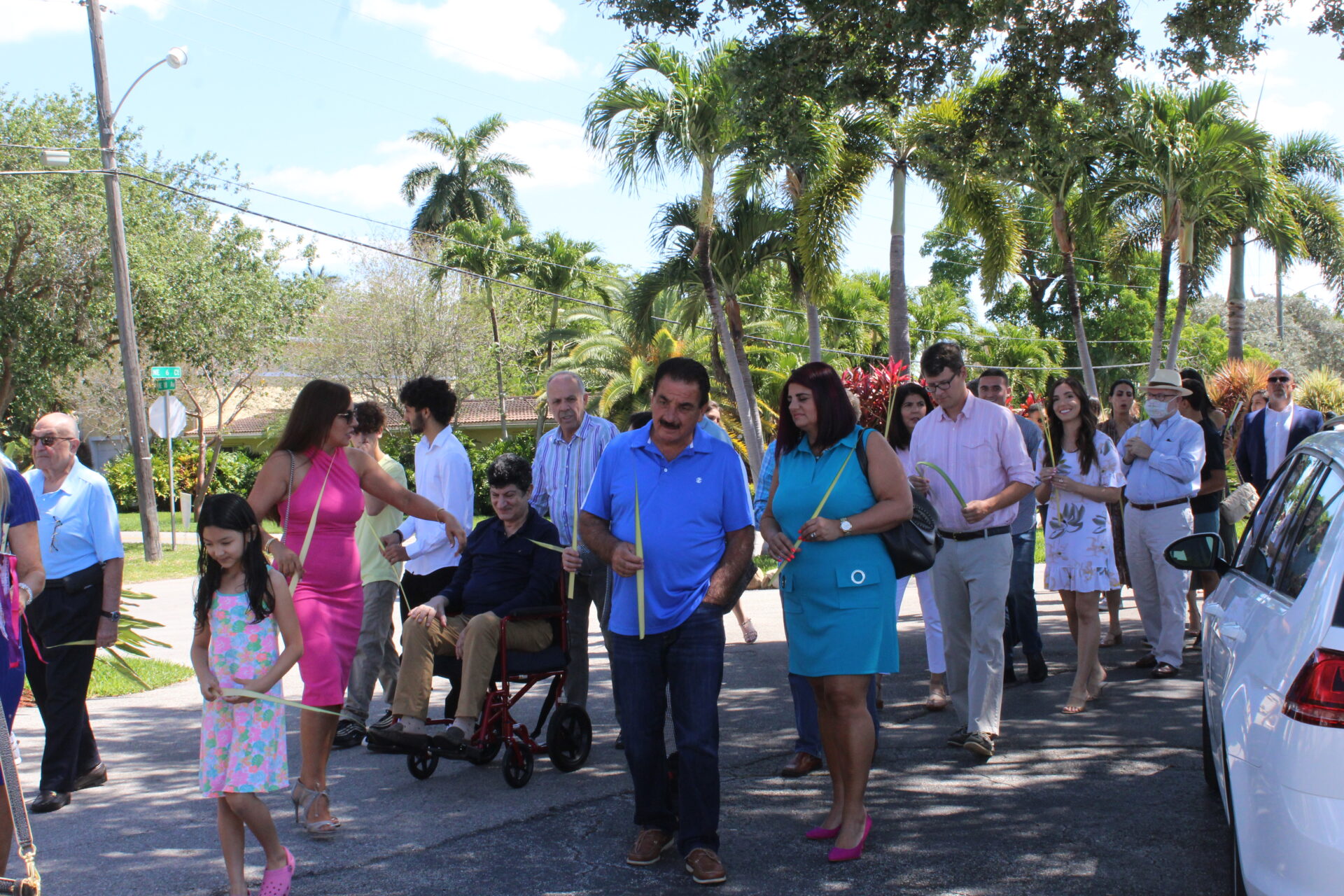 A man and woman wearing blue outfit while holding a piece of long palm leaf