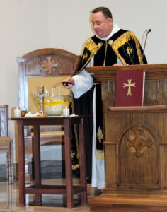 A priest wearing a black vest while lighting the candle near the glass cross