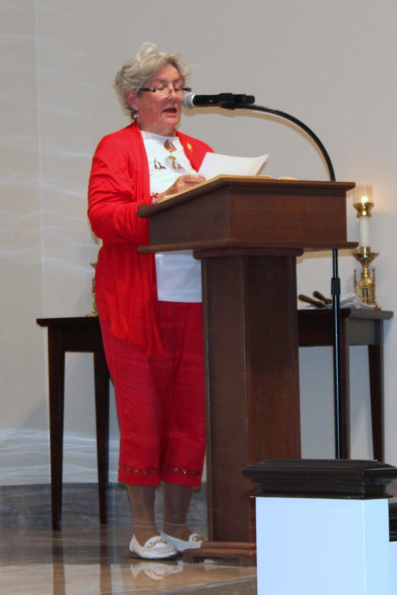 A woman wearing a white top and red cardigan with red pants and a pair of white shoes