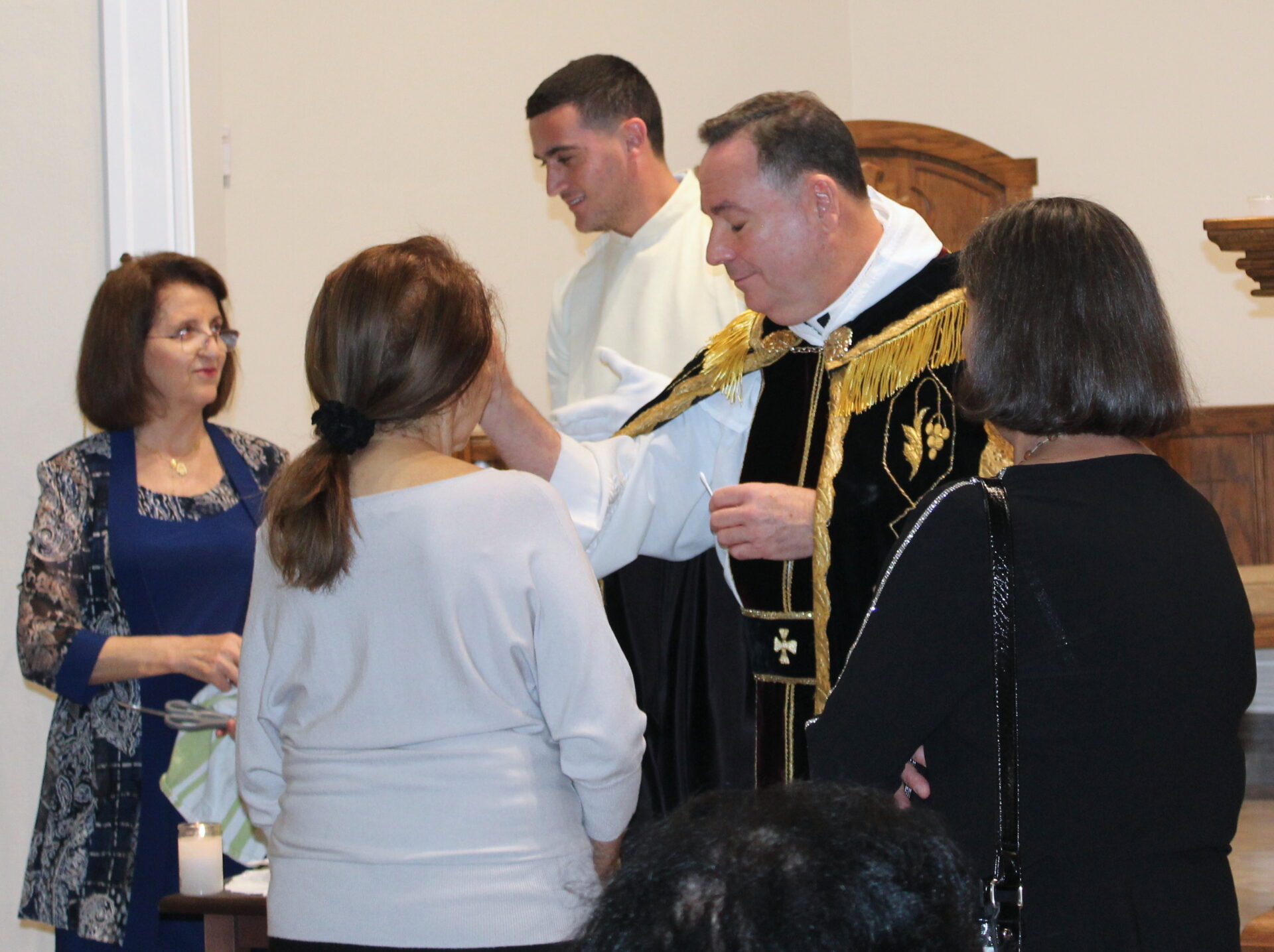 A woman with a black pony tail in front of the priest