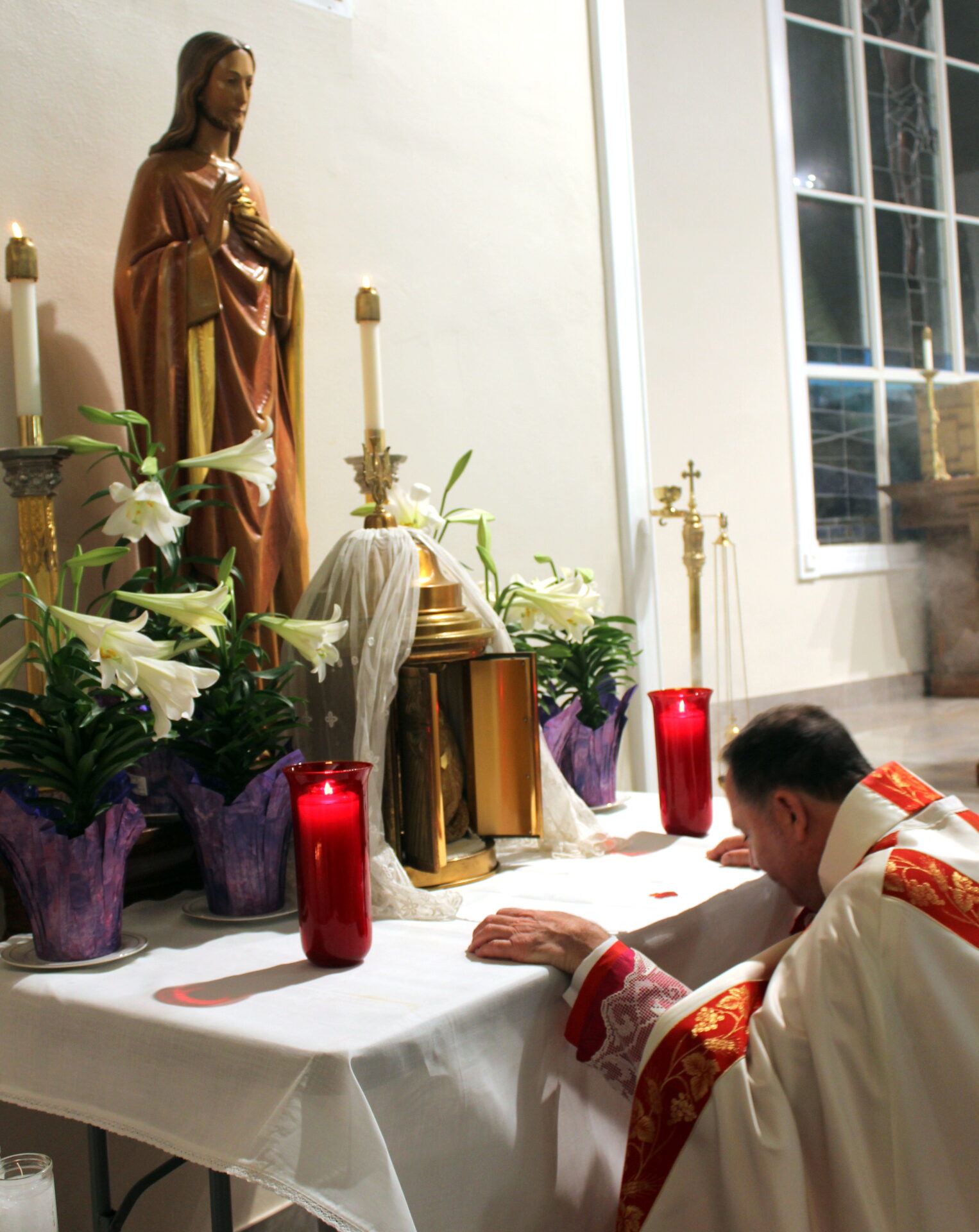 The priest kneeling down in front of the altar with two red candles