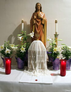 An altar with two candles, a statue, and four purple flower vases