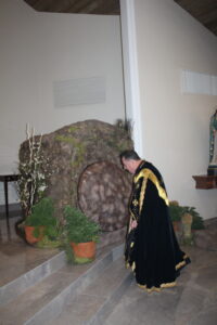 A priest wearing a black Pontifical vestment while looking down on a stone near the altar