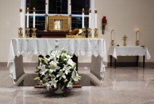 A church altar with white table clothes, white candles with gold stands, and a basket of white flowers